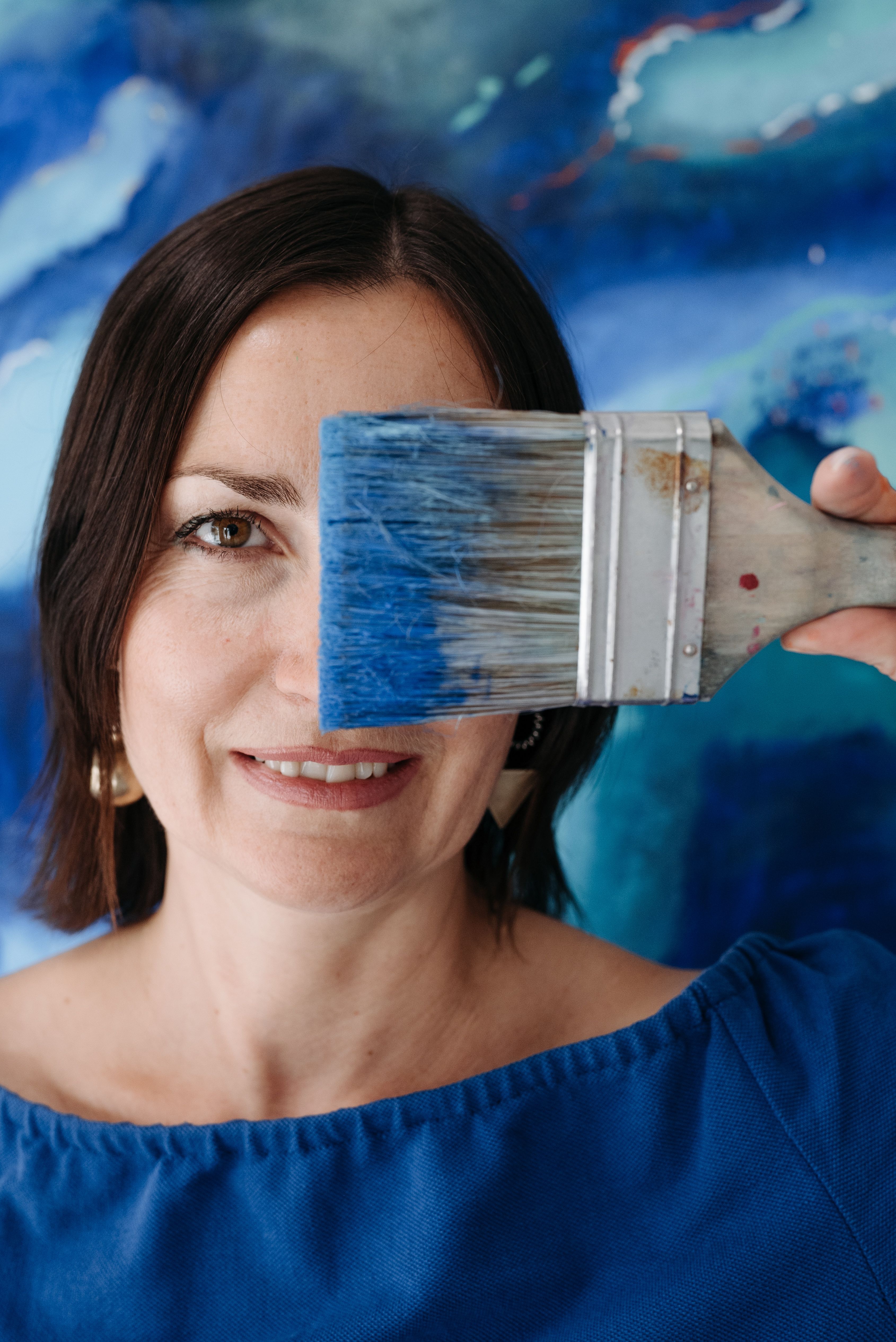 Artistic portrait of a smiling woman holding a paintbrush against a vibrant blue background