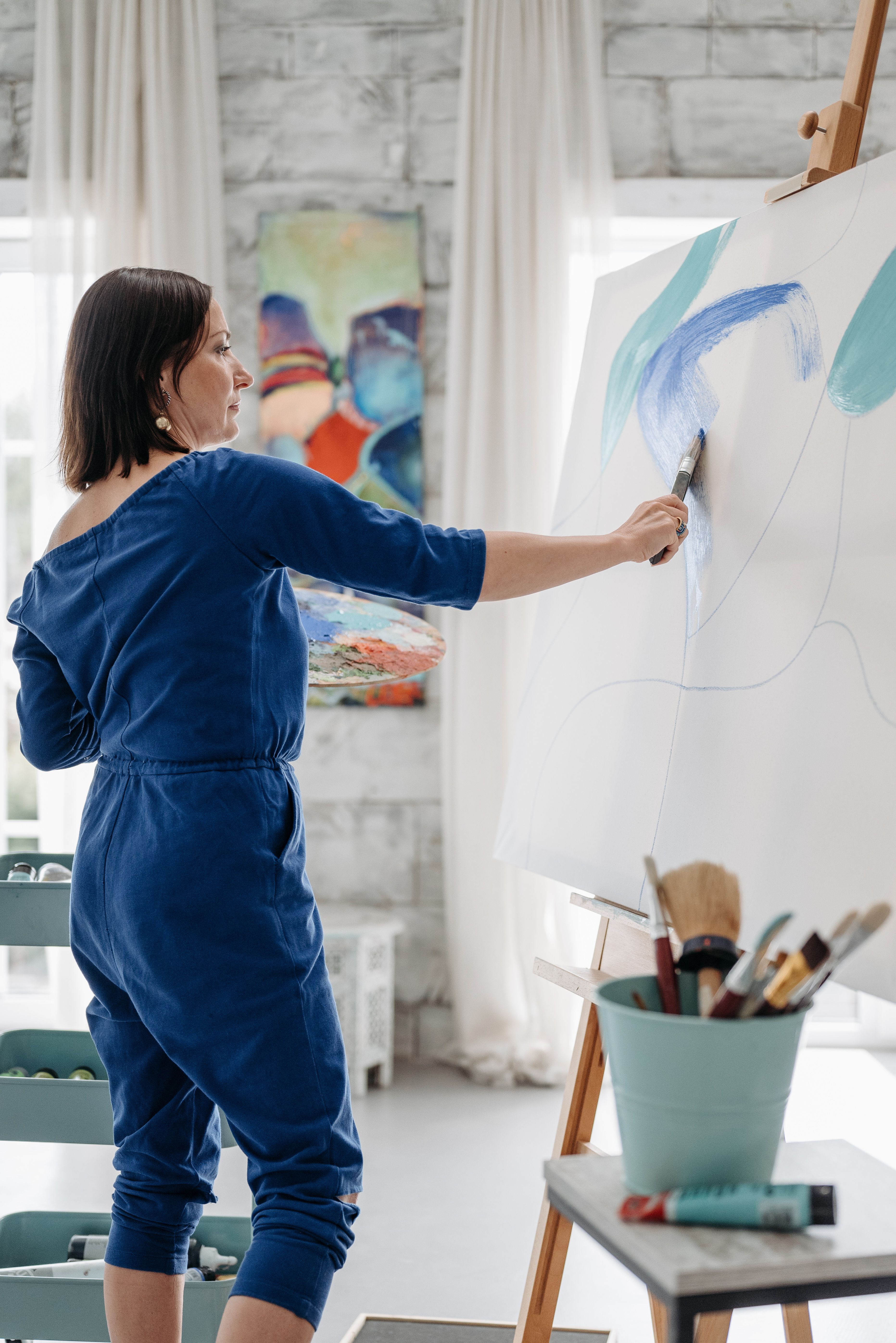 Artist in a blue jumpsuit painting a colourful abstract on a large canvas