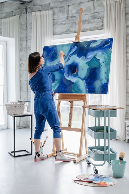 Free A woman artist painting a vibrant abstract blue artwork on canvas in a modern art studio. Stock Photo