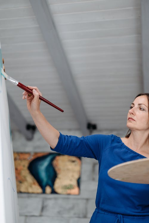 Woman Holding a Palette and a Paintbrush and Painting on Canvas 