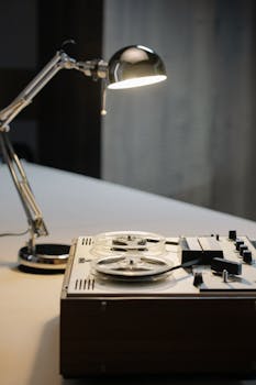 A classic reel-to-reel tape recorder paired with a stylish desk lamp in a vintage setting.