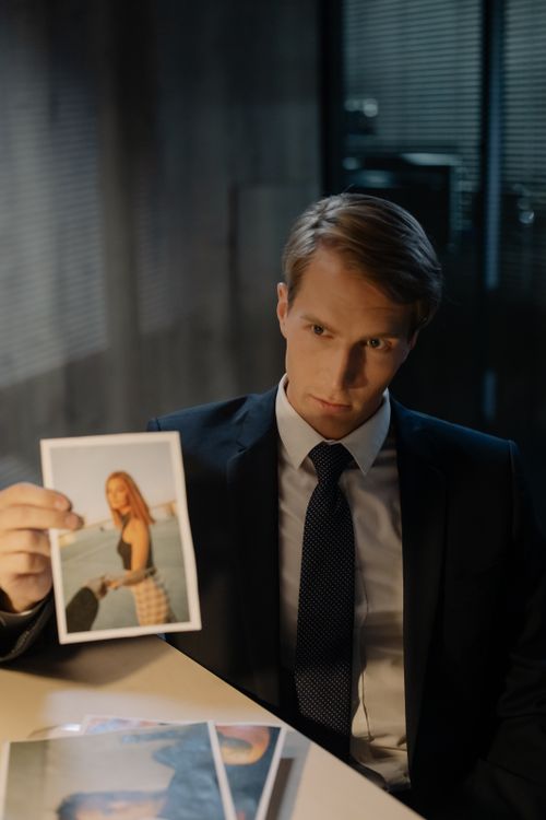 Free A detective in a suit analyzes a photograph during an investigation in a dimly lit office. Stock Photo