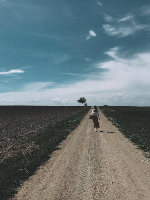 A Woman Carrying a Basket Walking on the Dirt Road