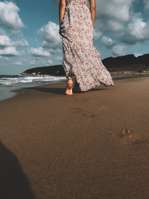 A Woman in a Floral Dress Walking on the Shore