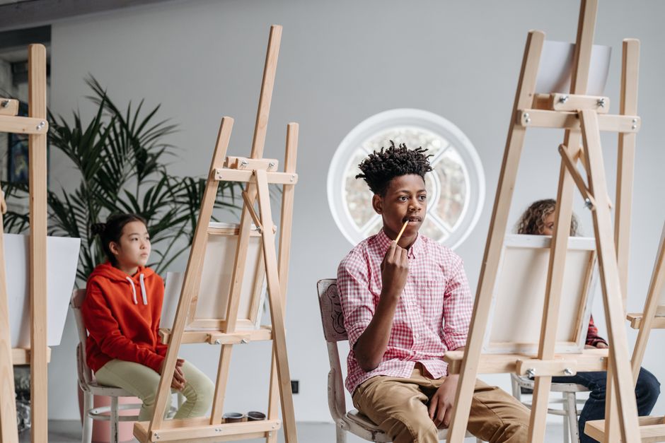 Children of diverse backgrounds participate in an art lesson with easels in a classroom setting.