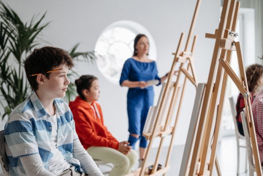 Children attentively participate in an art class, learning painting with easels and a teacher's guidance.