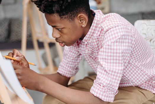 Teen boy drawing with focus in a creative indoor setting wearing checkered sleeves.