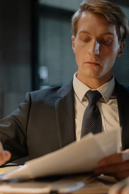 A focused detective examining papers at a desk in an office setting. A focused detective examining papers at a desk in an office setting.