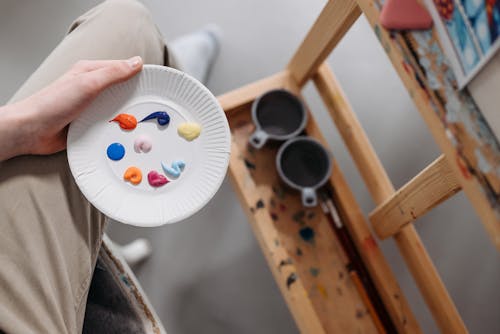 Top View of Person Sitting by an Easel and Holding a Palette with Paint 