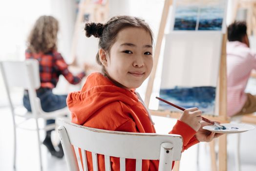 Asian girl smiles as she paints in an art class, embracing creativity.