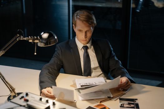 Focused investigator reviewing evidence in a dimly lit office setting.