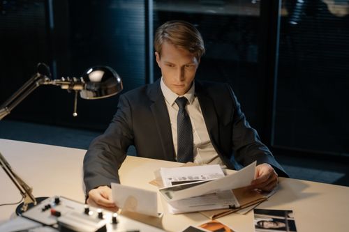 Free Focused investigator reviewing evidence in a dimly lit office setting. Stock Photo