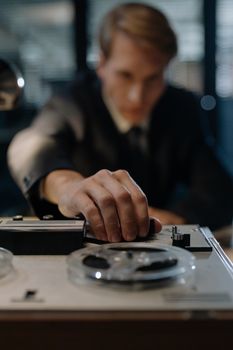 A focused man operating a vintage tape recorder with shallow focus and soft lighting.