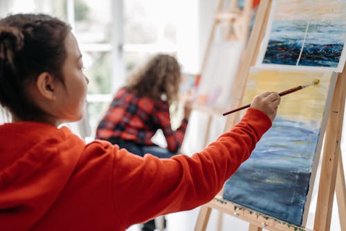 A Girl in Orange Jacket Painting on the Canvas