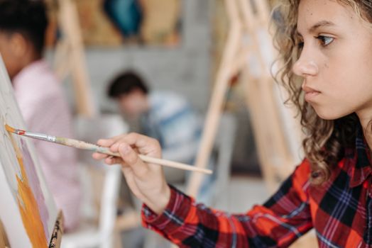 Young girl deeply focused on painting at an art class, capturing creativity and education indoors.