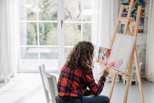 Free A person painting on a canvas in a bright, sunlit studio with large windows. Stock Photo