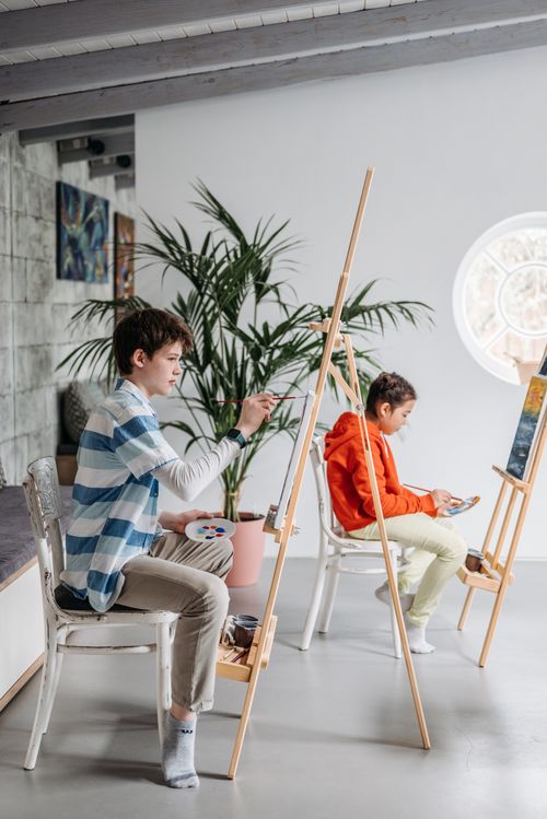 Free Two children painting on easels in a bright, indoor art class environment. Stock Photo