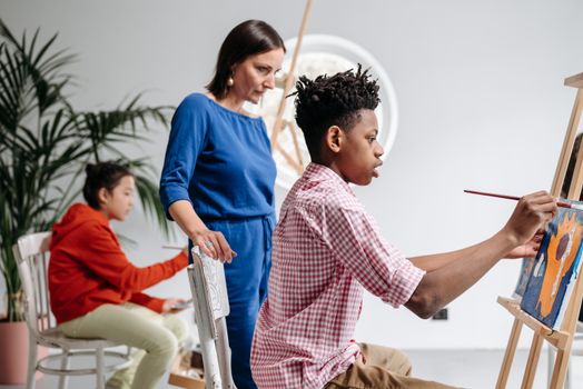 Dynamic art class scene with teacher guiding young students as they paint on canvases.