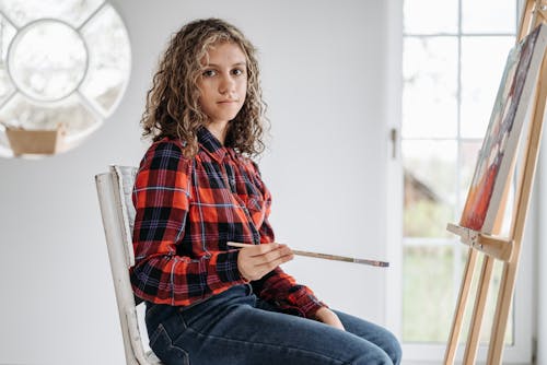 Girl Holding a Paintbrush Sitting by an Easel with Canvas 