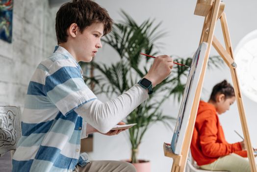 Two children painting in an art class, focused on creativity and learning indoors.