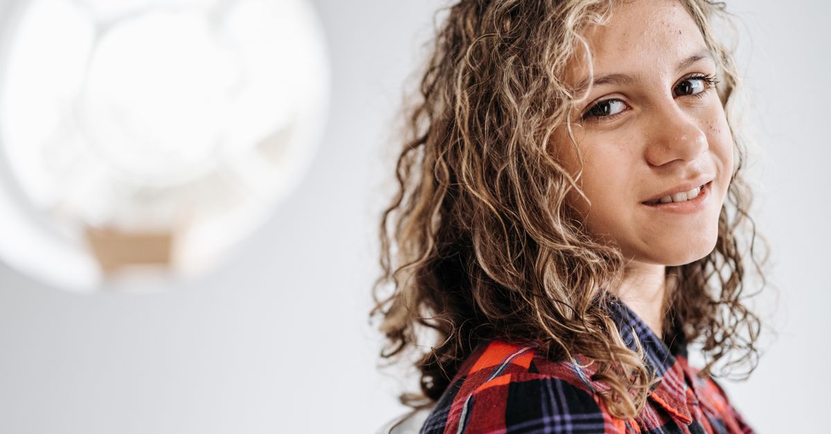 Portrait of a young girl smiling indoors wearing a checkered shirt.