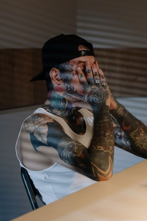 Free A tattooed man in a cap covers his face, expressing emotion and mystery. Stock Photo