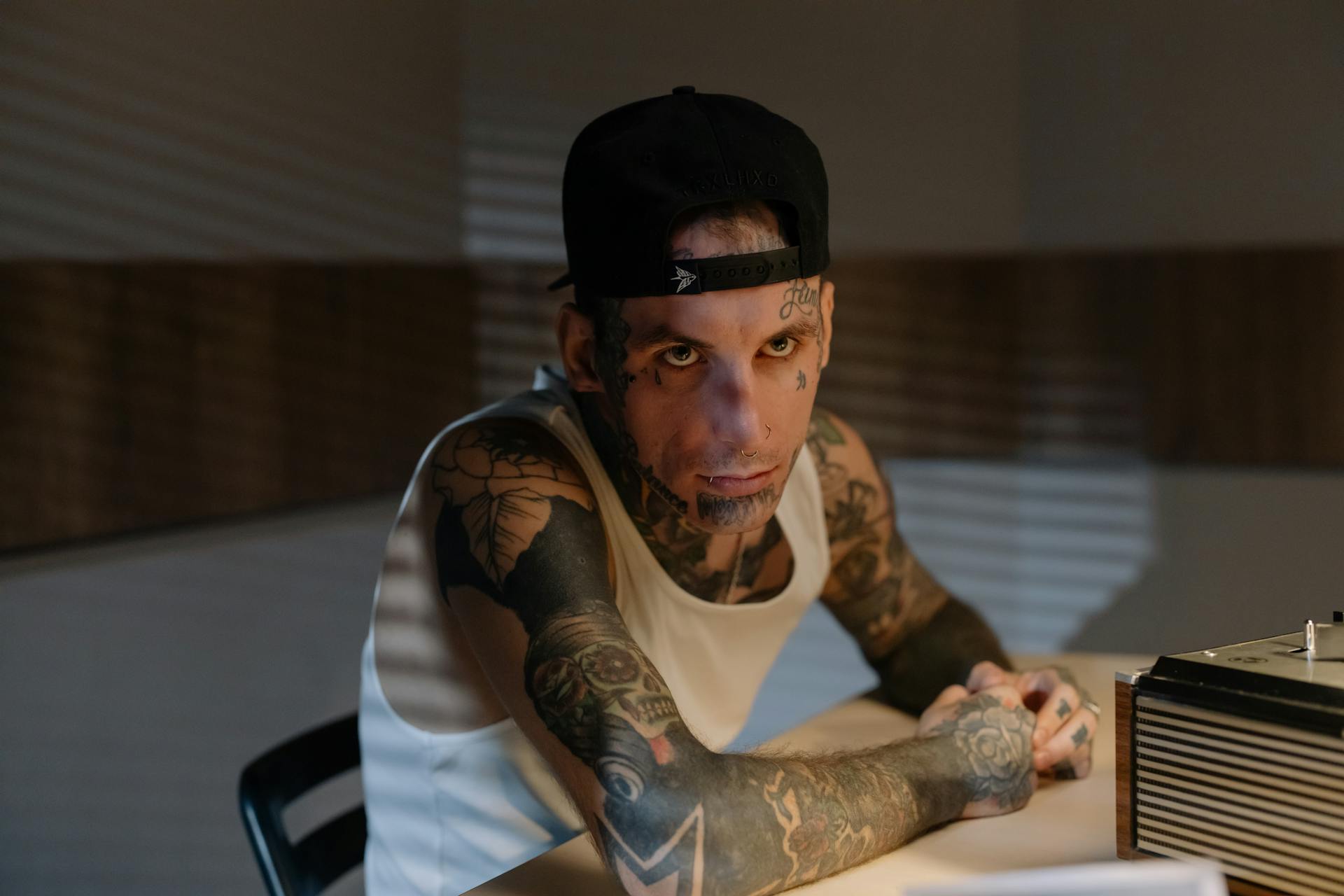 Tattooed man with intense look in a dimly lit interrogation room.