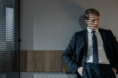 Free Businessman in suit, relaxed in office with dynamic shadow patterns from window blinds. Stock Photo