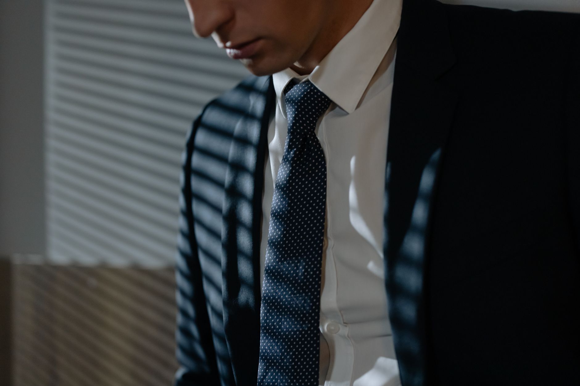 Close-up of a man in a suit and tie under striped shadows, evoking a corporate feel.