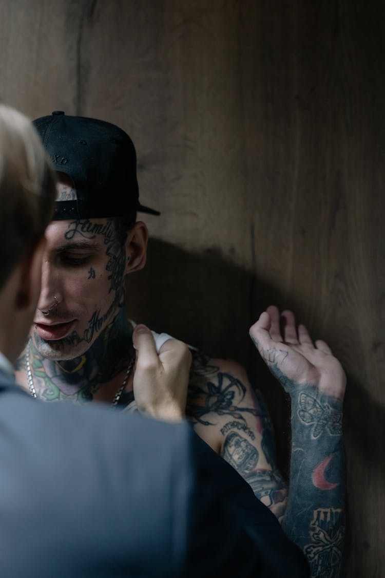 A Man With Face And Arm Tattoo Against A Wooden Wall