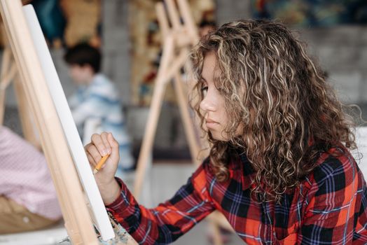 A young woman with curly hair and a plaid shirt focused on sketching in an art class.