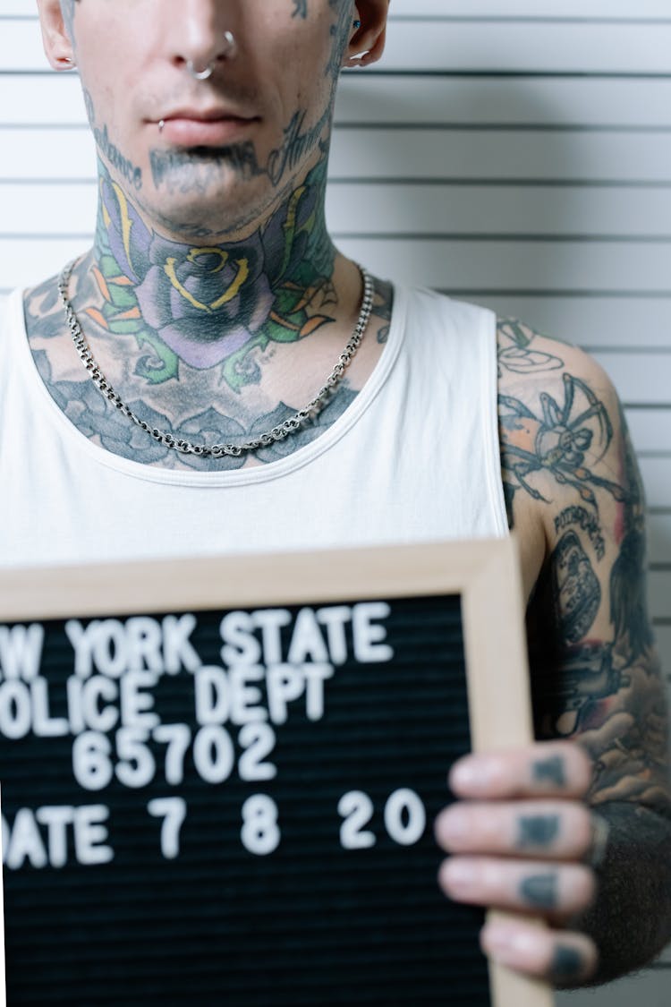 Close-up Of A Tattooed Man Holding A Board On A Mugshot