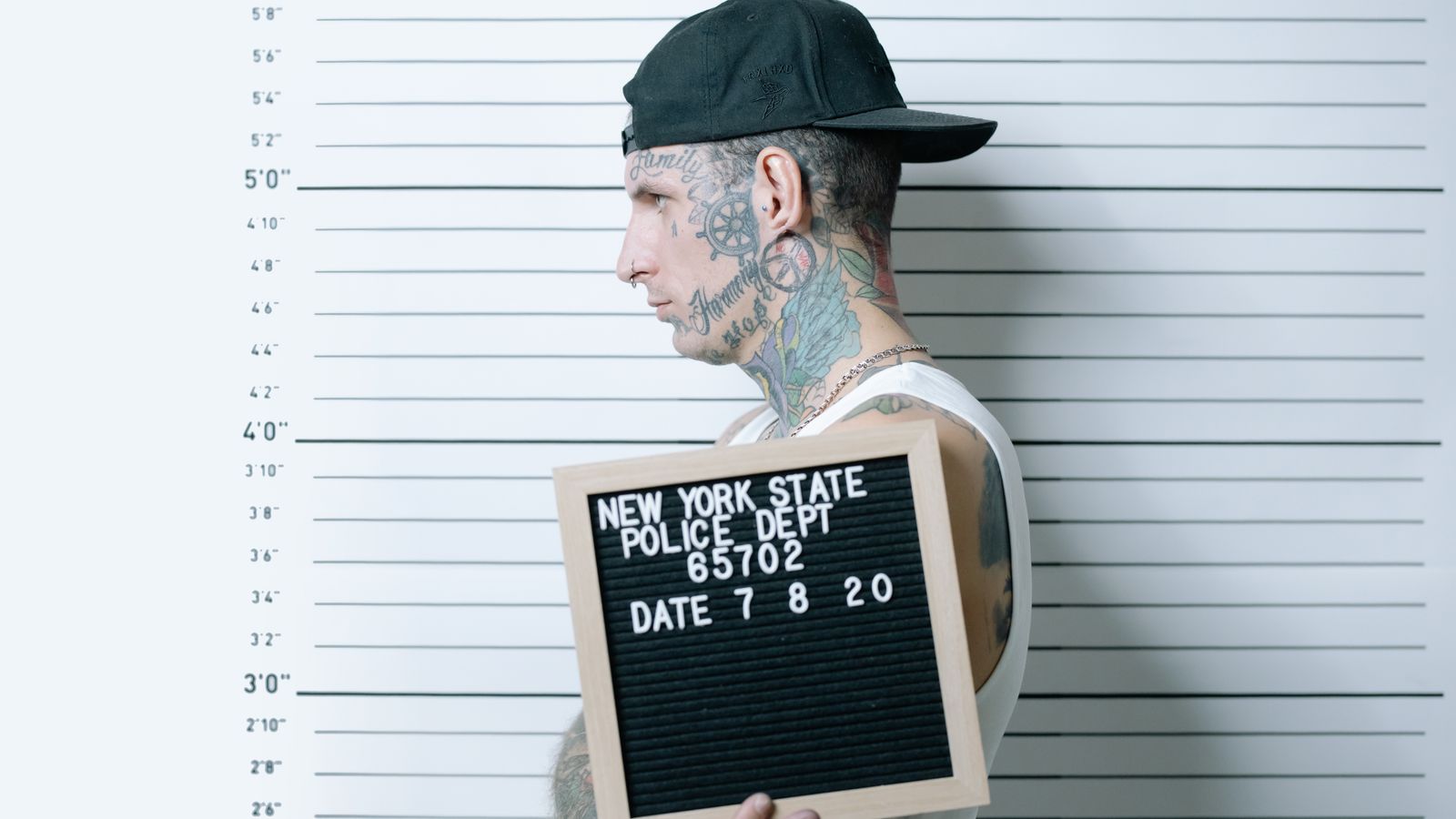 Side view of tattooed man holding mugshot board in police lineup.