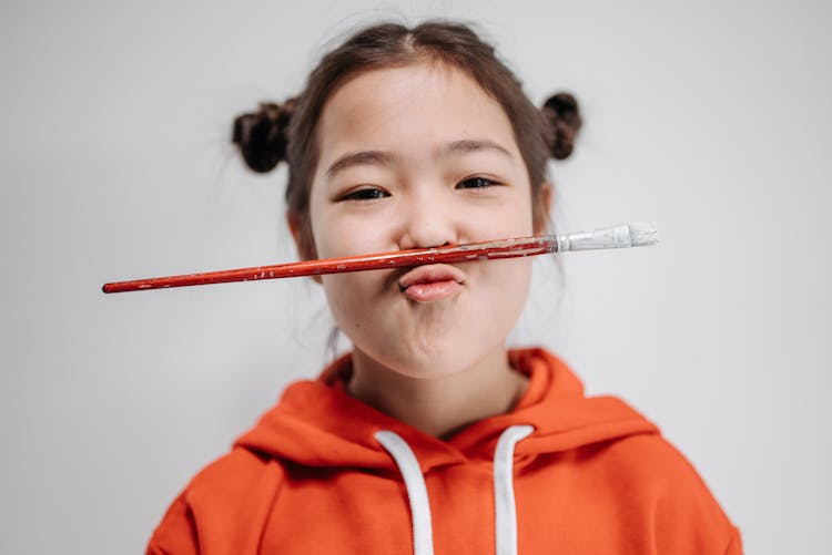 Young Girl Balancing A Paintbrush On Her Upper Lip 