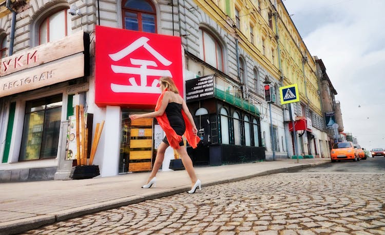 A Woman In A Black Dress And Red Scarf Crossing The Street