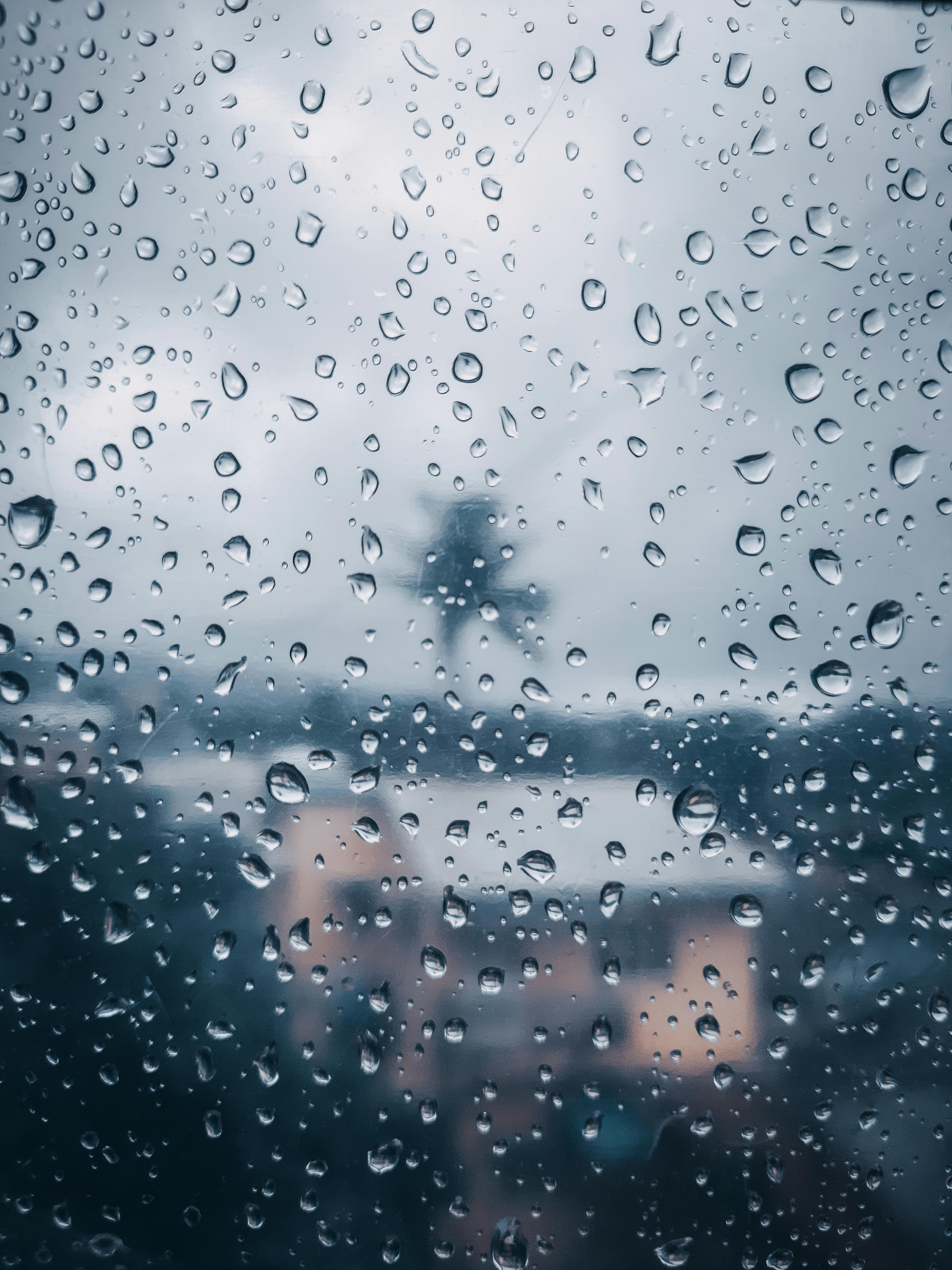 View through raindrop-covered window revealing a blurred cityscape in soft light.