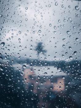 View through raindrop-covered window revealing a blurred cityscape in soft light.