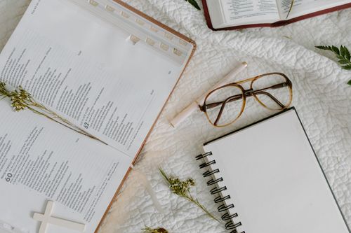 Free An open Bible with glasses and a blank notebook on a cozy bedspread setting. Stock Photo