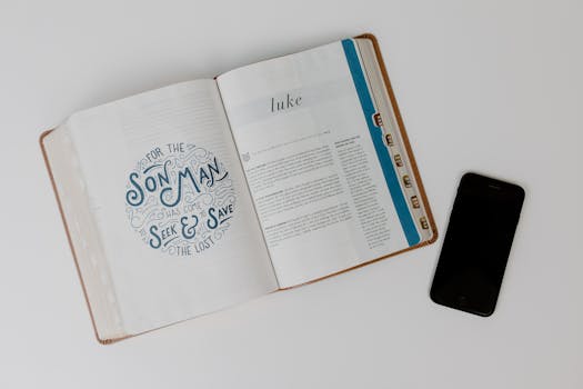 Open Bible displaying the Book of Luke next to a smartphone on a white surface.
