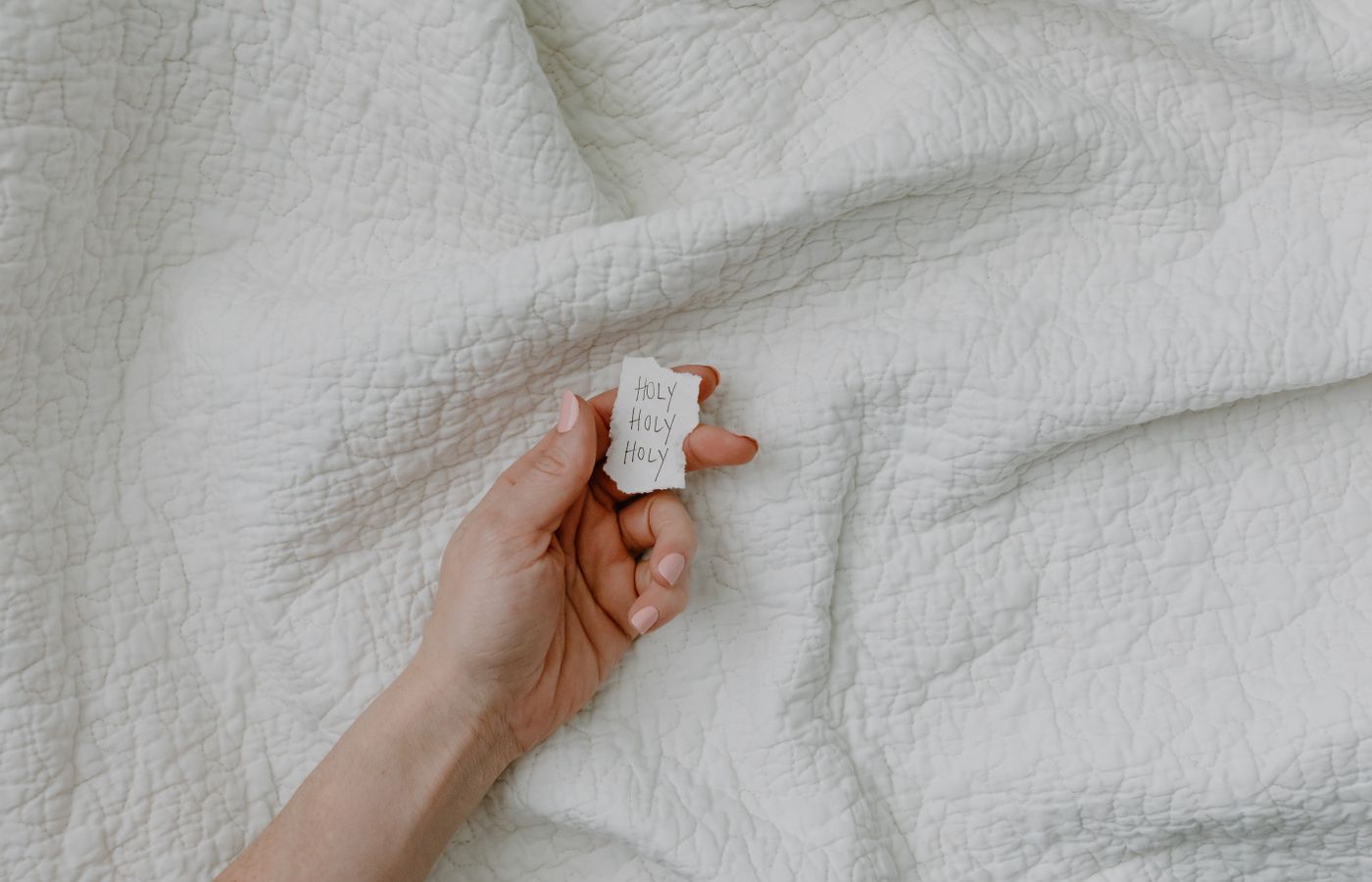 A hand with manicured nails holds a handwritten inspirational note against a textured fabric background.