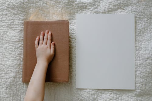 A Child's Hand on a Journal beside a Blank Piece of Paper