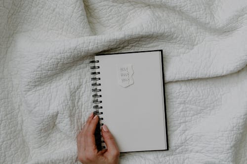 Person Holding White Spiral Notebook on White Fabric