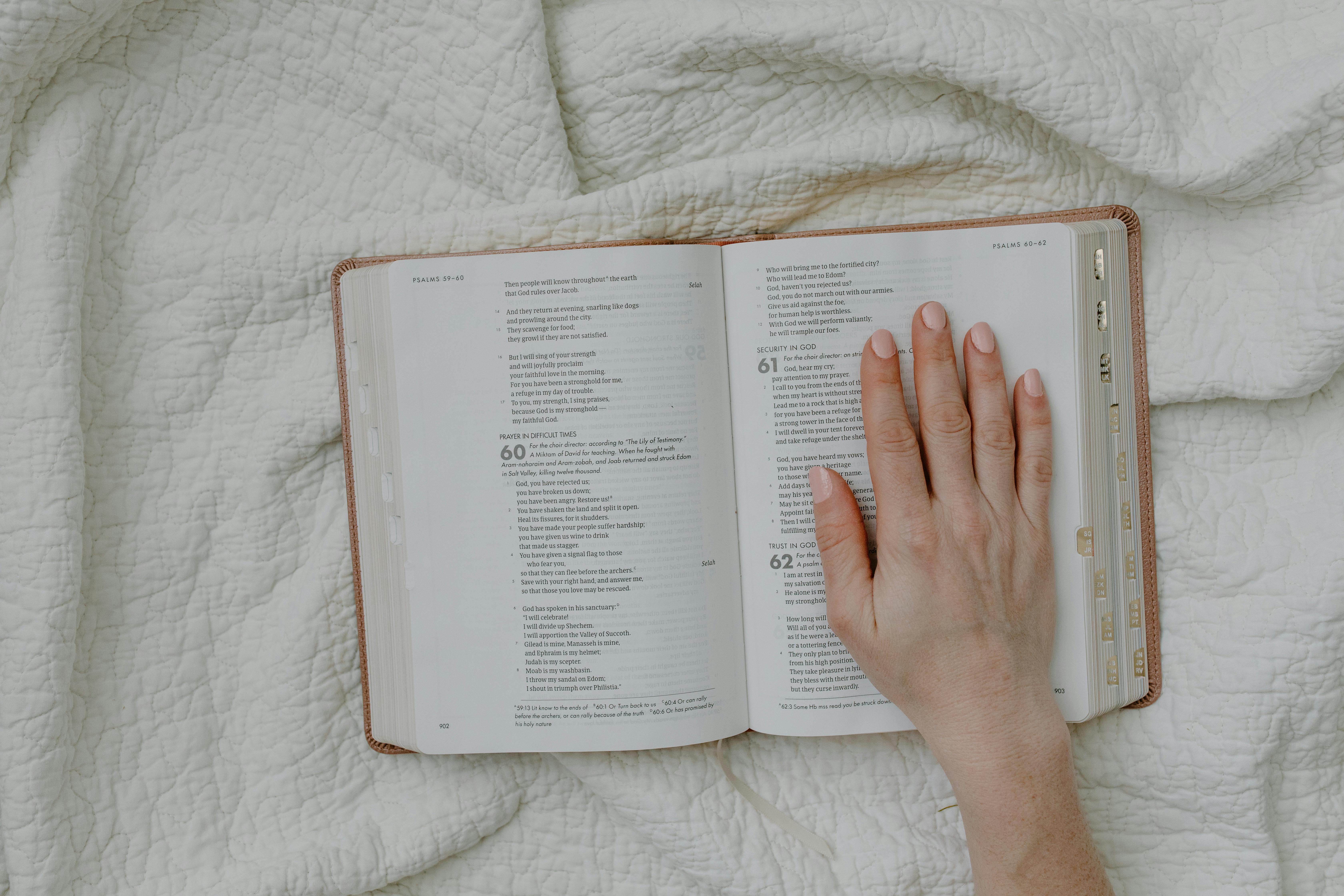 A hand rests on an open Bible set against a soft quilted fabric, offering a serene religious scene.