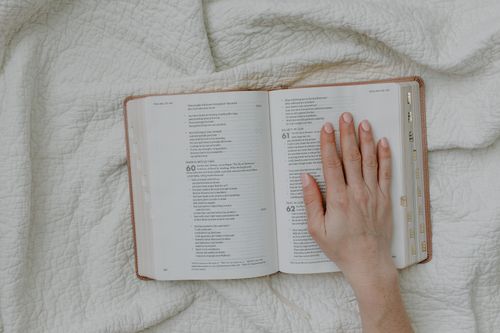 Free A hand rests on an open Bible set against a soft quilted fabric, offering a serene religious scene. Stock Photo