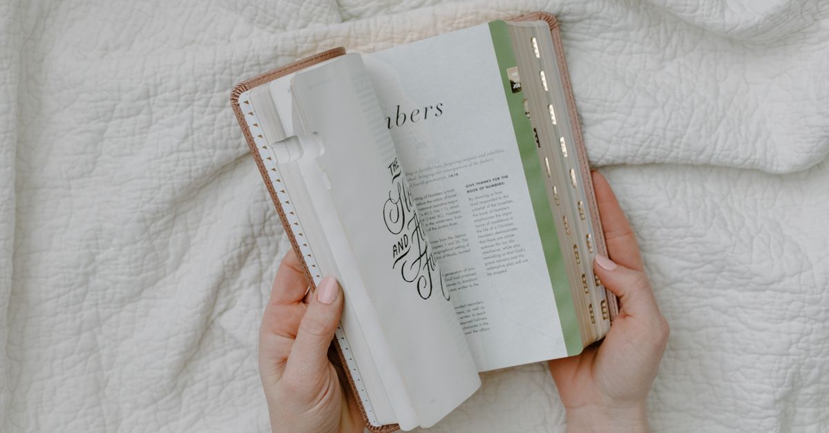 close-up of hands holding an open Bible with a magnifying glass resting on the pages