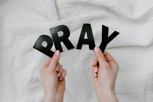 Free Close-up of hands holding black cutout letters spelling PRAY on white fabric background. Stock Photo
