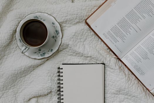 Flat lay of a coffee cup, open Bible, and notebook on a quilted fabric, creating a cozy and serene scene.