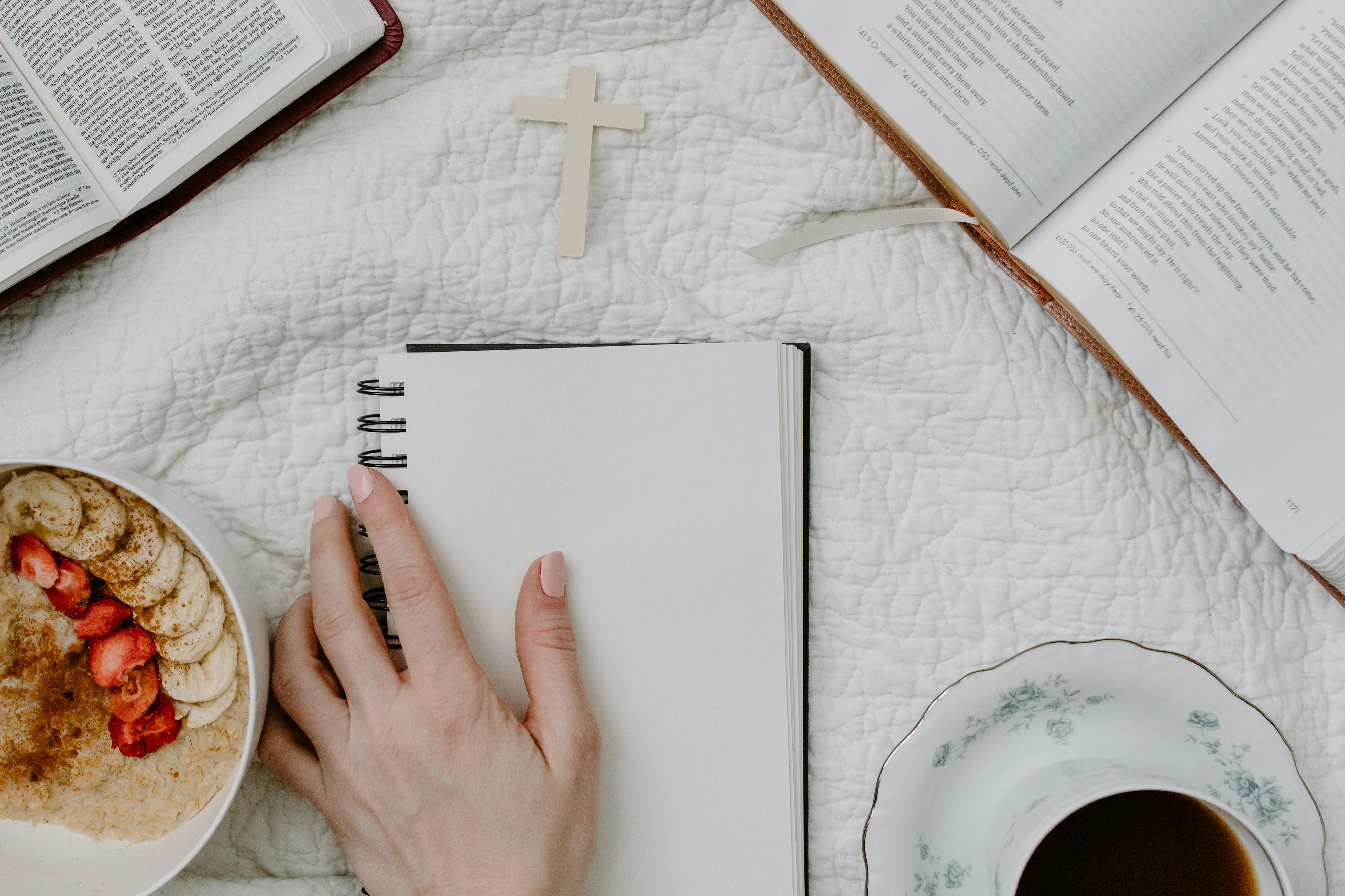 a person holding a blank notebook beside the books and bowl of cereal