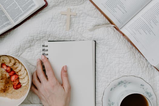 Top view of a morning devotional setup with bible, coffee, and notebook on a cozy textile background.