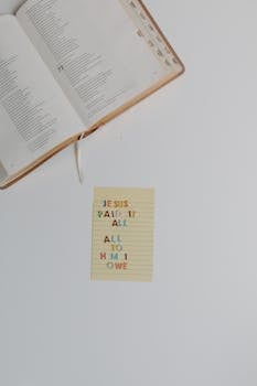 A flat lay of an open bible with a note stating 'Jesus paid it all, all to him I owe'.